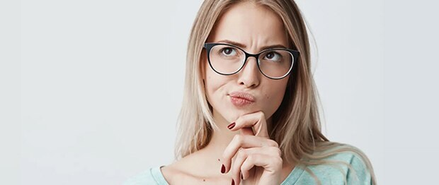 Een blonde vrouw met een bril raakt nadenkend haar kin aan